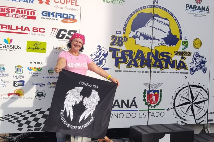 Telma Crummenauer posa com a bandeira das Filhas do Vento e da Liberdade no pódio do Transparaná 2022. Foto: arquivo pessoal